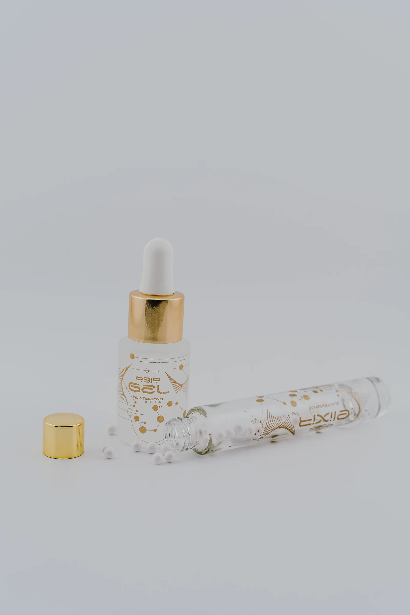 An open QBio Elixir vial with white beads beside a gold-collar QBio Gel bottle.
