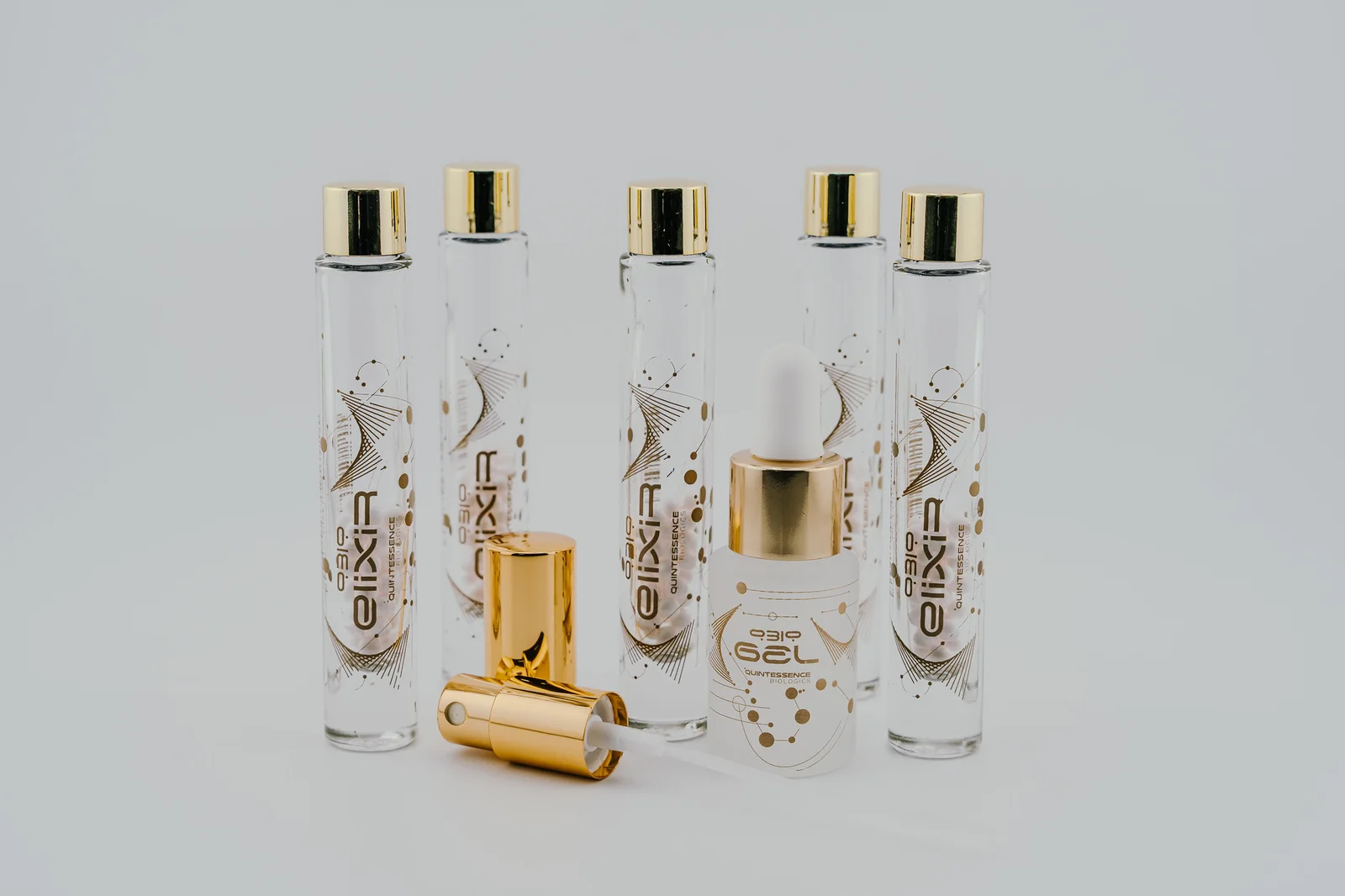 Five gold-capped QBio Elixir vials, QBio Gel and the photographed mister and cap.